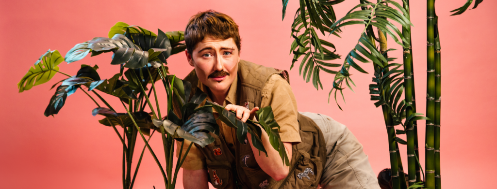 Bi Curious George against a pink background amongst some leafy plants