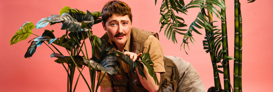 Bi Curious George against a pink background amongst some leafy plants