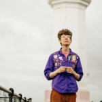 Hollie McNish support Michael Pedersen stood in front of a lighthouse wearing a purple shirt.