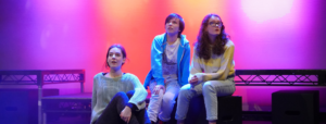 Brewery Youth Theatre, children sat on stage lit by pink and orange lights