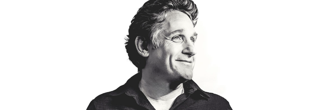 Tom Stade in black and white, smiling to the right on a white background