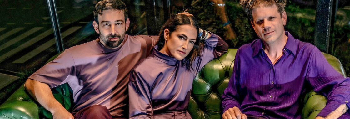 Joan As Police Woman band all wearing purple sat on a green sofa.