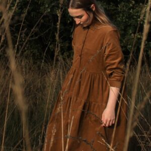 Woman wearing long brown cord button up dress in long grass field